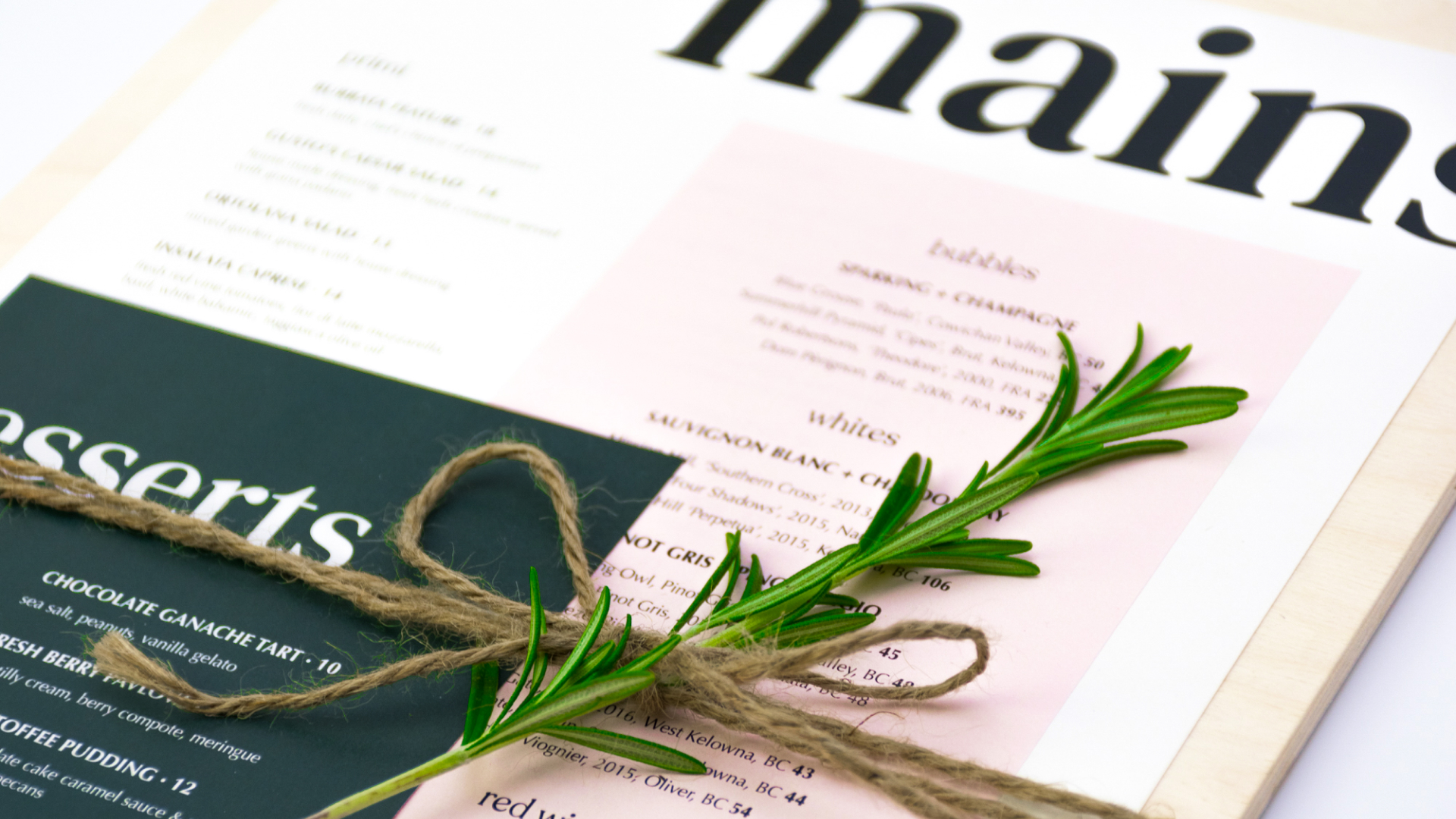 A menu set on a wooden board with a sprig of rosemary tied on top with twine.
