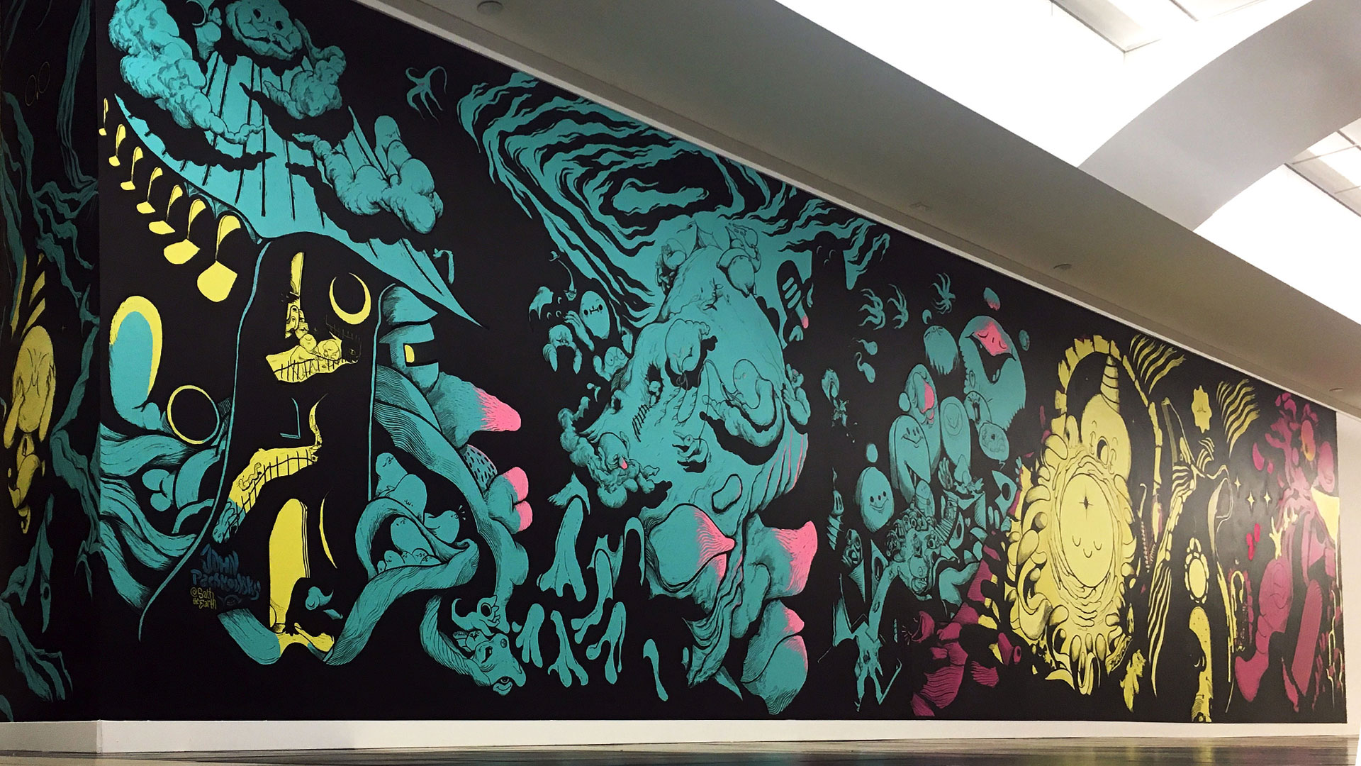A wide angle shot of the completed mural’s entire span in a brightly lit mall corridor.